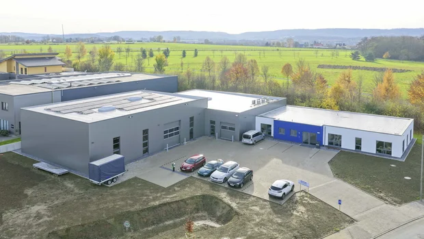 Produktionshalle mit angebautem Bürogebäude Luftaufnahme der neu errichteten Produktionshalle mit angebautem Bürogebäude, Parkfläche und moderner grauer und blauer Fassadengestaltung.